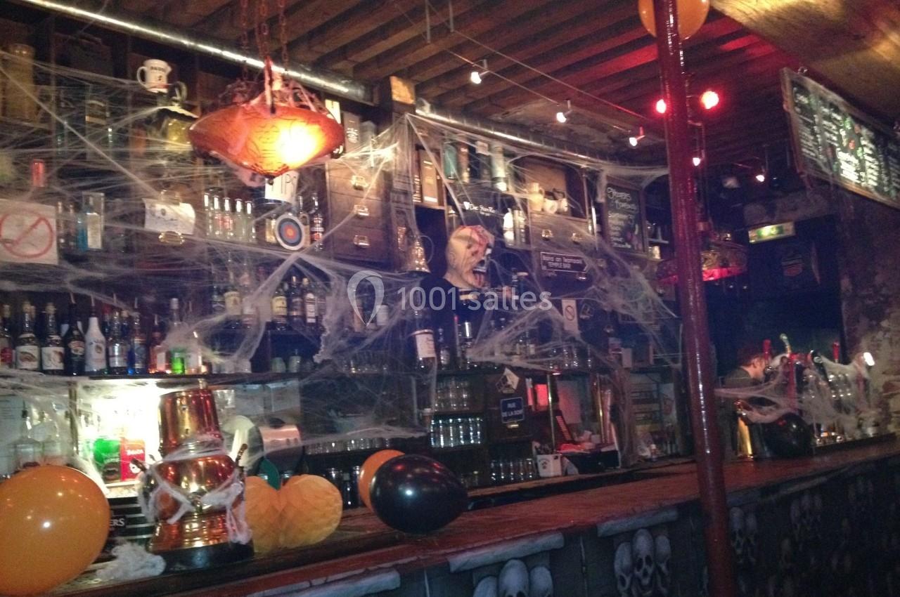 Bar décoré pour Halloween avec toiles d'araignées, ballons orange et noirs, et lumières tamisées.