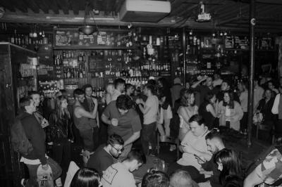 Intérieur d'un bar avec comptoir en bois, tabourets hauts, murs en pierre et éclairage tamisé.