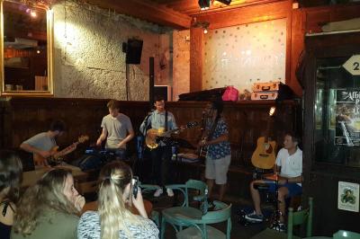 Intérieur d'un bar avec comptoir en bois, tabourets hauts, murs en pierre et éclairage tamisé.