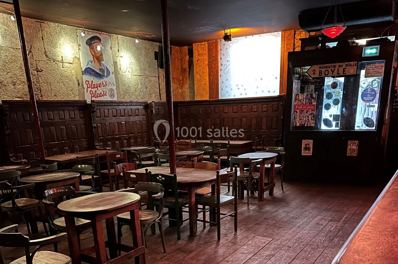 Salle de bar avec tables et chaises en bois, éclairage tamisé et décoration murale rétro.