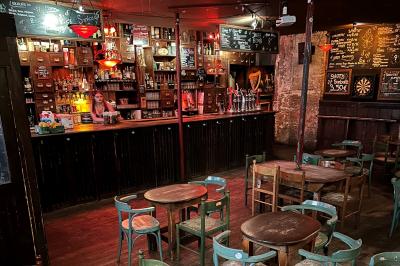 Intérieur d'un bar avec comptoir en bois, tabourets hauts, murs en pierre et éclairage tamisé.