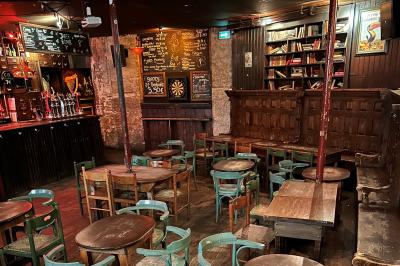 Intérieur d'un bar avec comptoir en bois, tabourets hauts, murs en pierre et éclairage tamisé.