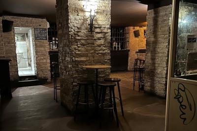 Intérieur d'un bar avec murs en pierre, tables hautes en bois, éclairage tamisé et porte de sortie de secours visible.