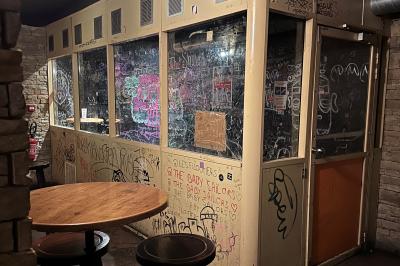 Intérieur d'un bar avec murs en pierre, tables hautes en bois, éclairage tamisé et porte de sortie de secours visible.