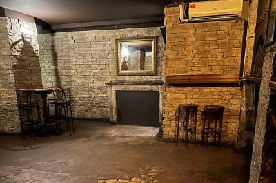 Intérieur d'un bar avec murs en pierre, tables hautes en bois, éclairage tamisé et porte de sortie de secours visible.