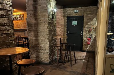 Intérieur d'un bar avec murs en pierre, tables hautes en bois, éclairage tamisé et porte de sortie de secours visible.