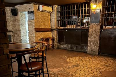 Intérieur d'un bar avec murs en pierre, tables hautes en bois, éclairage tamisé et porte de sortie de secours visible.