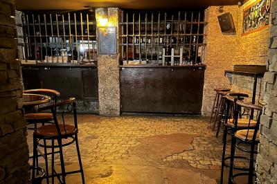 Intérieur d'un bar avec murs en pierre, tables hautes en bois, éclairage tamisé et porte de sortie de secours visible.