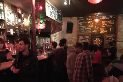 Intérieur d'un bar avec murs en pierre, tables hautes en bois, éclairage tamisé et porte de sortie de secours visible.