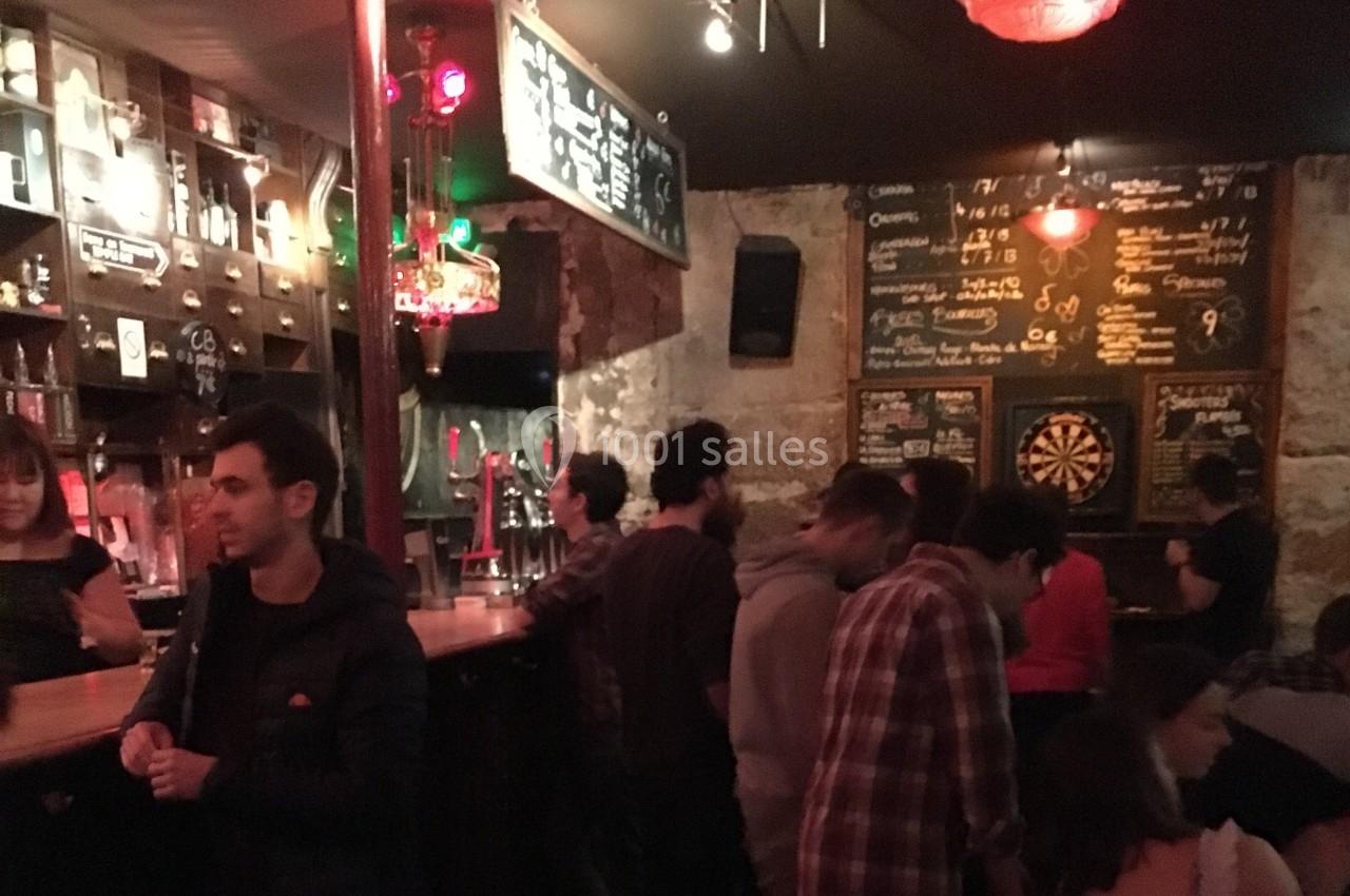 Des personnes discutent et commandent au comptoir d'un bar à l'ambiance tamisée avec des murs en pierre et un tableau de…