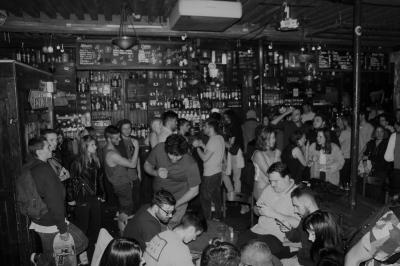 Intérieur d'un bar avec murs en pierre, tables hautes en bois, éclairage tamisé et porte de sortie de secours visible.