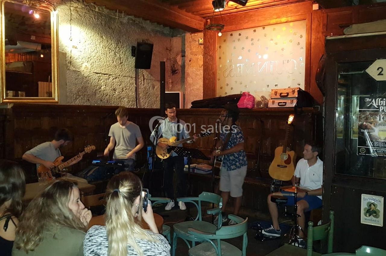 Un groupe de musiciens joue en live dans un bar, avec un public assis devant eux.
