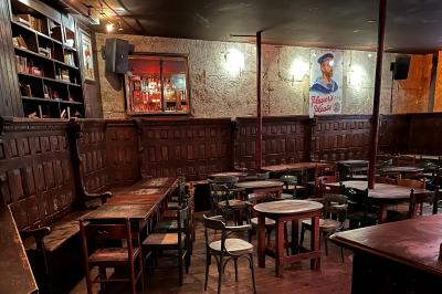 Intérieur d'un bar avec murs en pierre, tables hautes en bois, éclairage tamisé et porte de sortie de secours visible.