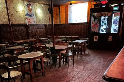 Intérieur d'un bar avec murs en pierre, tables hautes en bois, éclairage tamisé et porte de sortie de secours visible.