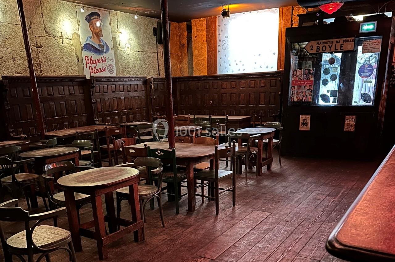 Salle de café ou bar avec tables et chaises en bois, éclairage tamisé et affiches décoratives sur les murs.