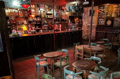 Intérieur d'un bar avec murs en pierre, tables hautes en bois, éclairage tamisé et porte de sortie de secours visible.
