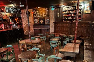 Intérieur d'un bar avec murs en pierre, tables hautes en bois, éclairage tamisé et porte de sortie de secours visible.