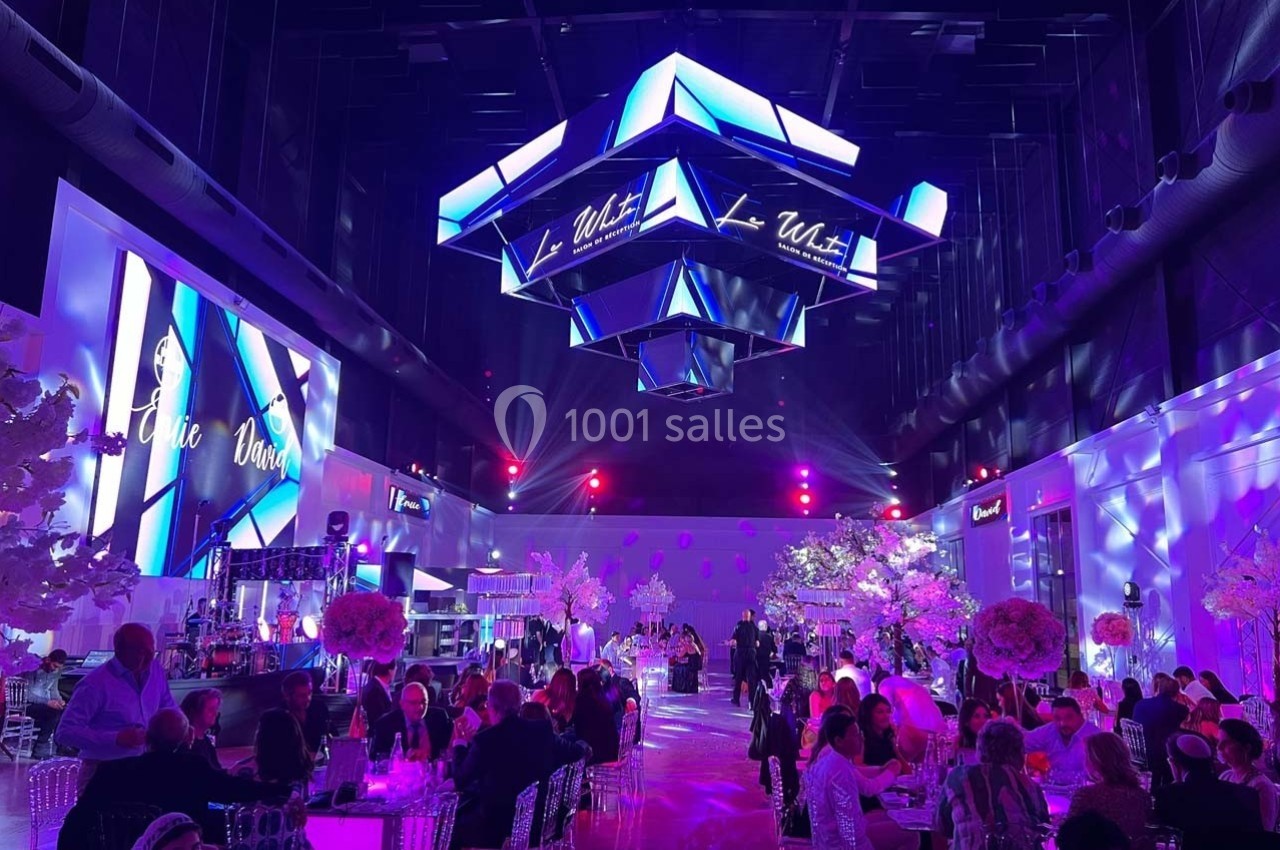Salle de réception illuminée de lumières violettes et bleues, avec des invités assis à des tables décorées.