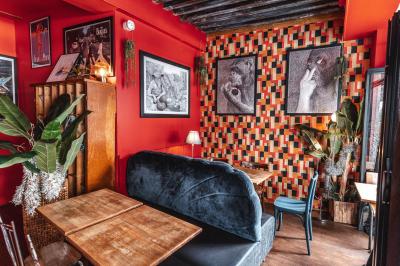 Terrasse de café avec tables et chaises alignées sur un trottoir, bordée de plantes et devantures de magasins.