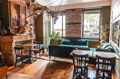 Terrasse de café avec tables et chaises alignées sur un trottoir, bordée de plantes et devantures de magasins.