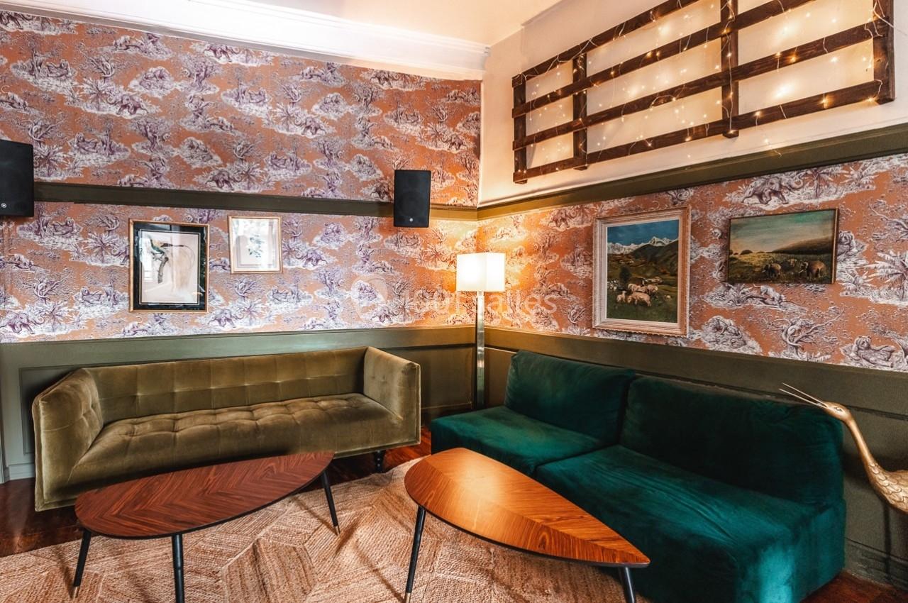 Salon décoré avec des canapés verts, tables en bois, murs tapissés et éclairage chaleureux.