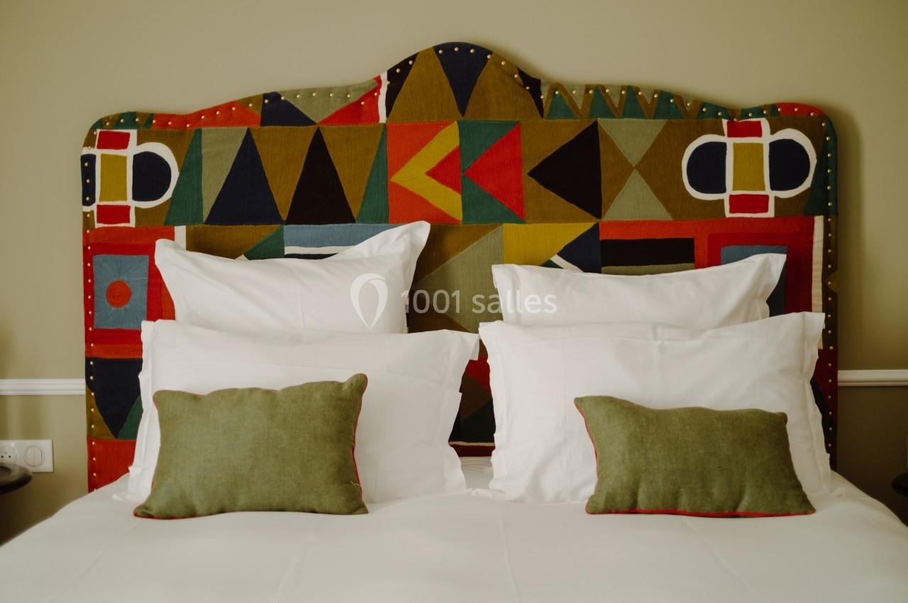 Lit avec tête de lit colorée à motifs géométriques, deux oreillers blancs et deux coussins verts.