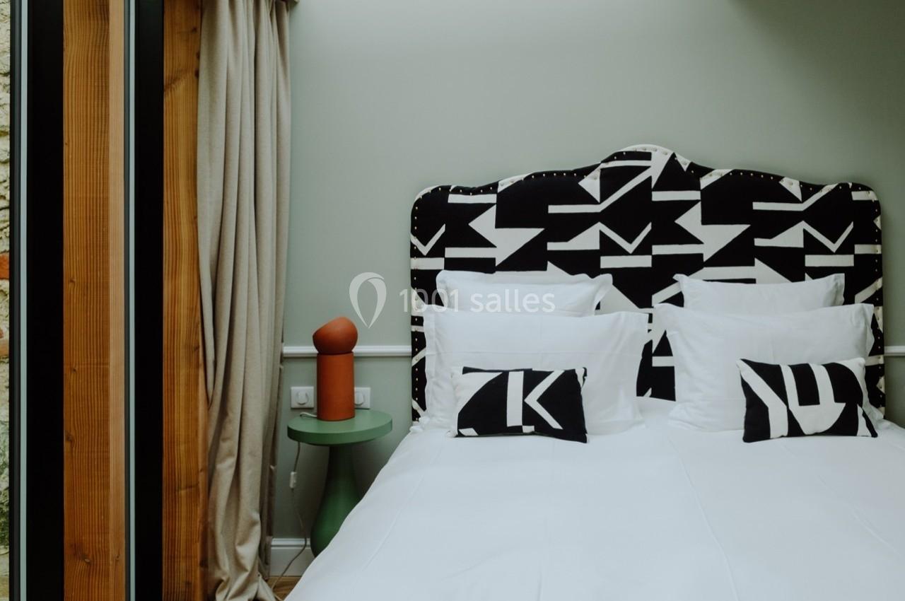 Lit double avec tête de lit noire et blanche à motifs géométriques, deux coussins assortis et table de chevet verte.