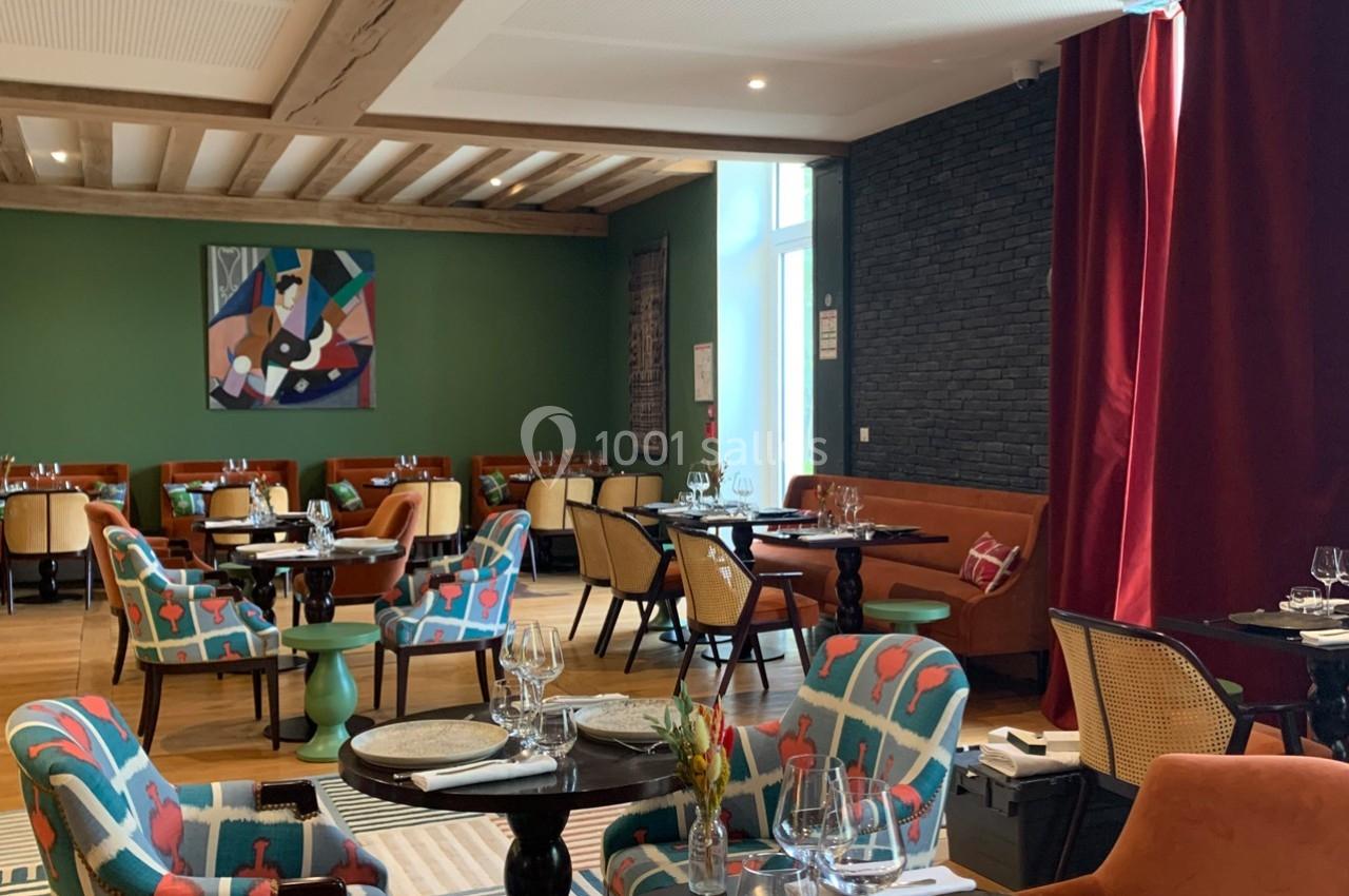 Salle de restaurant lumineuse avec des tables dressées, des fauteuils colorés et une décoration moderne.