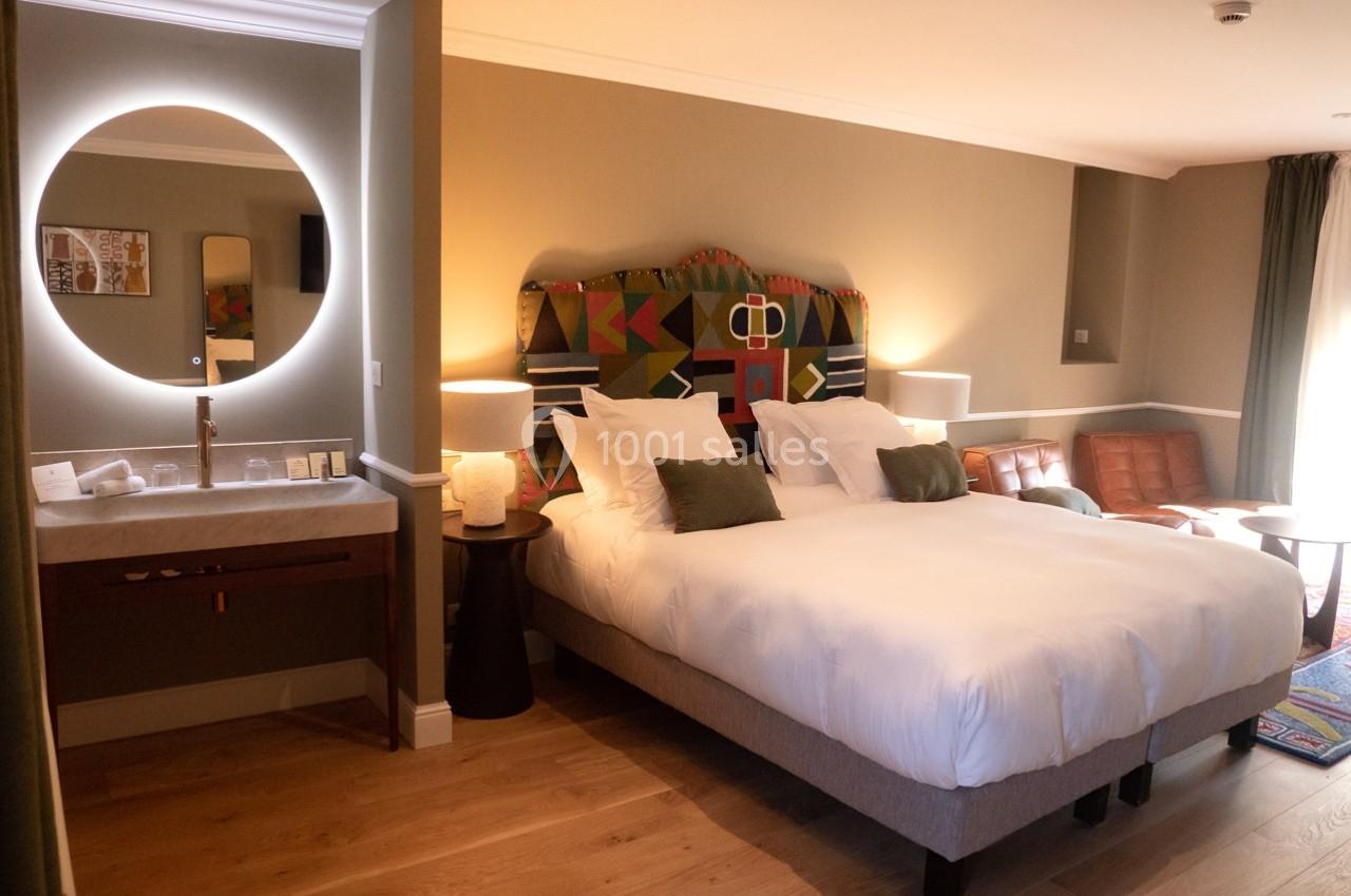 Chambre d'hôtel avec lit double, tête de lit colorée, coin salon, lavabo éclairé et parquet en bois clair.