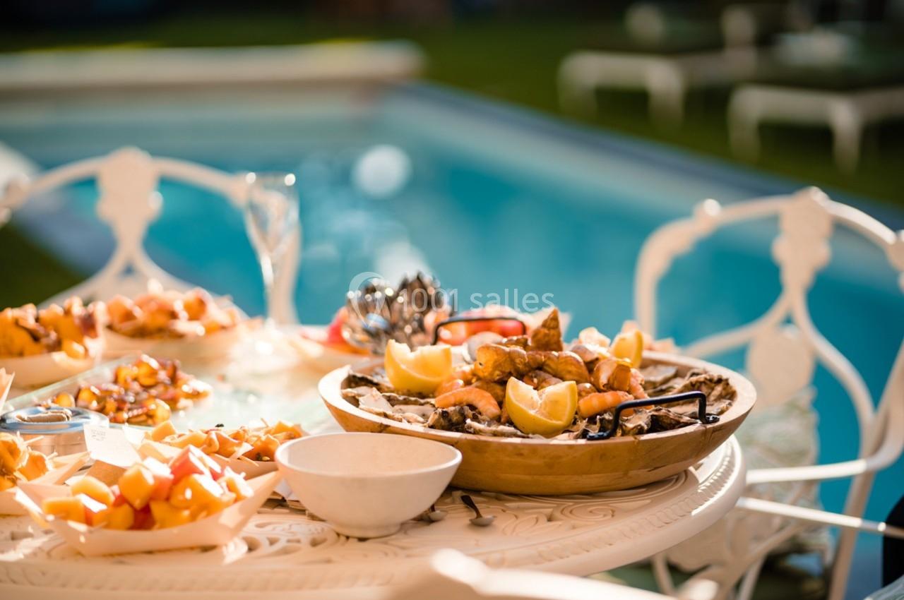 Plateau de fruits de mer et plats variés disposés sur une table en extérieur près d'une piscine.