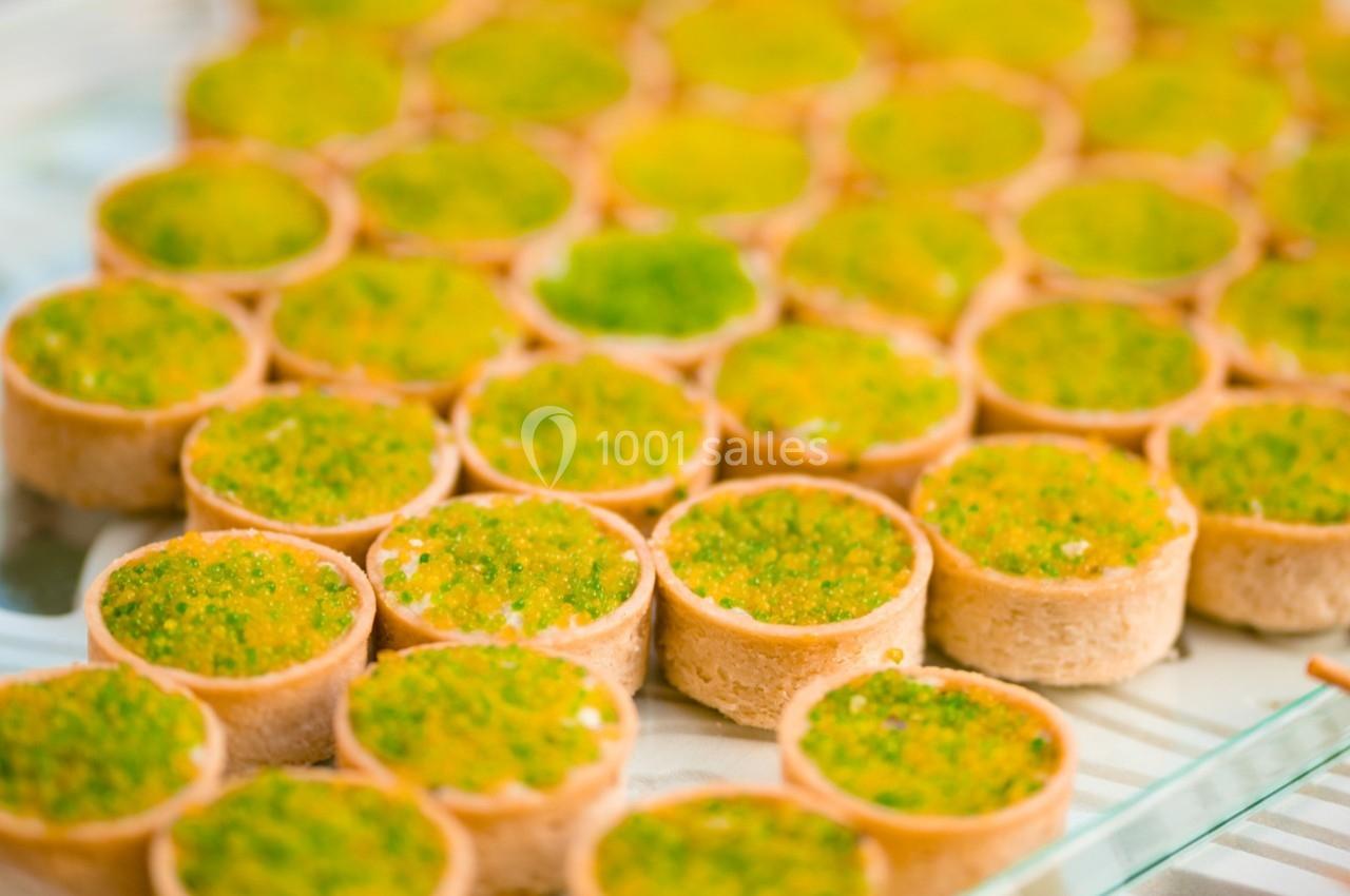 Petites tartelettes garnies d'une préparation verte, disposées en rangées sur une surface en verre.