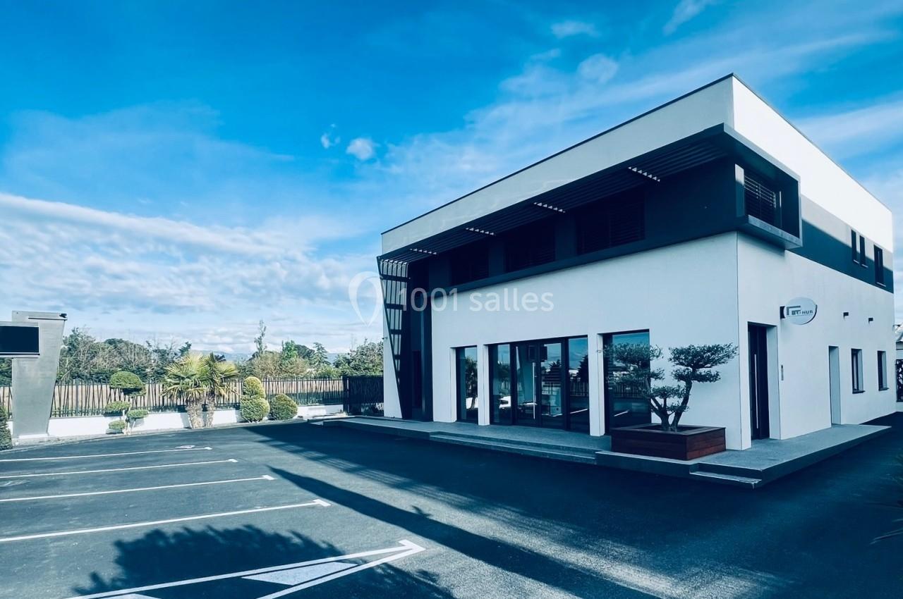 Bâtiment moderne blanc et noir avec parking vide, sous un ciel bleu dégagé.
