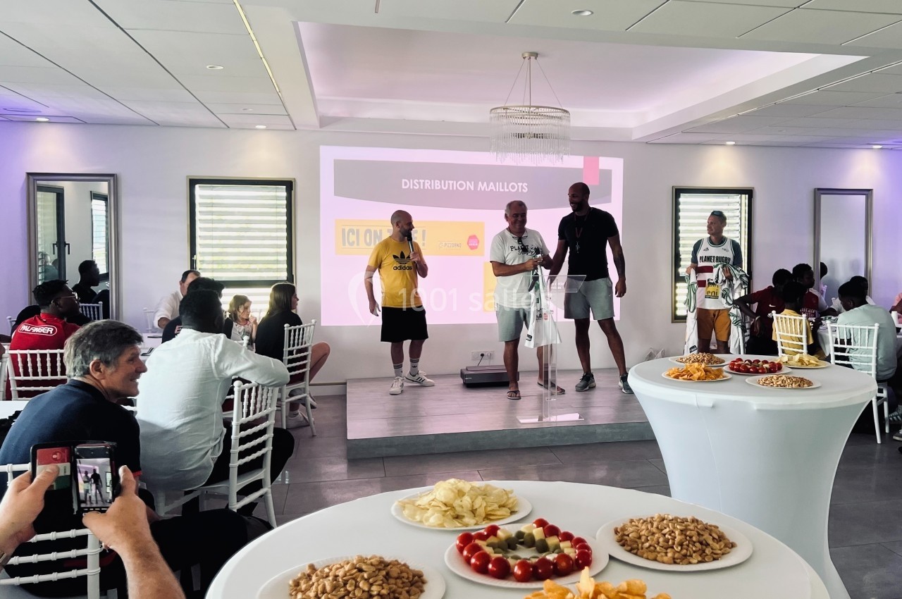 Des participants assistent à une remise de maillots dans une salle avec des tables garnies de collations au premier plan.