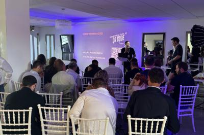 Des personnes assises assistent à une présentation dans une salle éclairée par des lumières violettes.