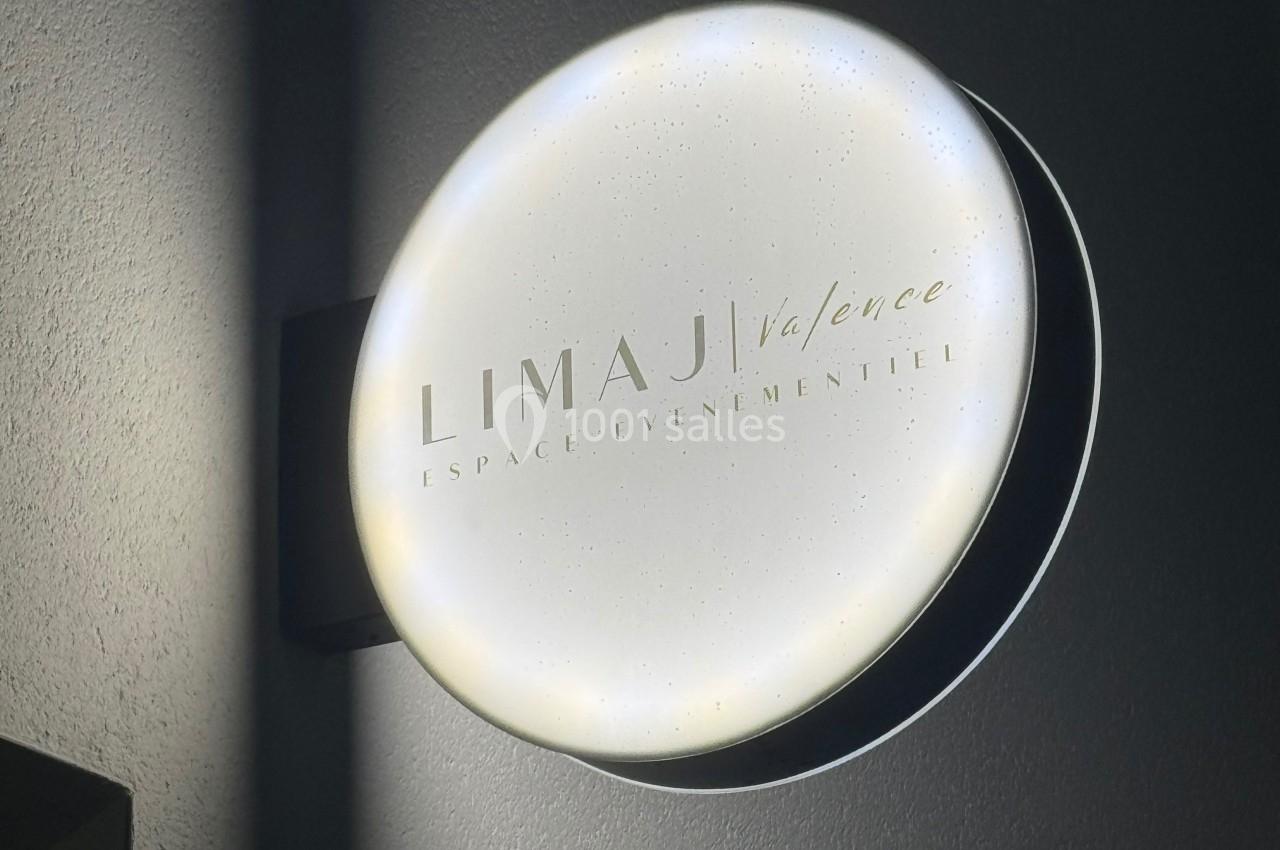 Enseigne lumineuse ronde indiquant ’Limaji Valence, espace événementiel’ fixée sur un mur sombre.