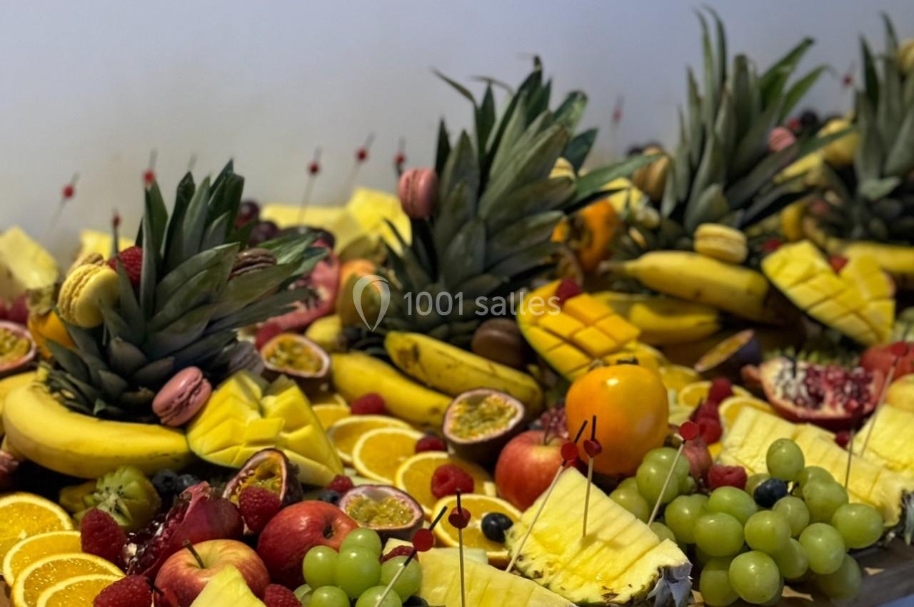 Plateau de fruits variés avec ananas, oranges, raisins, bananes, fruits de la passion et grenades sur une table en bois.