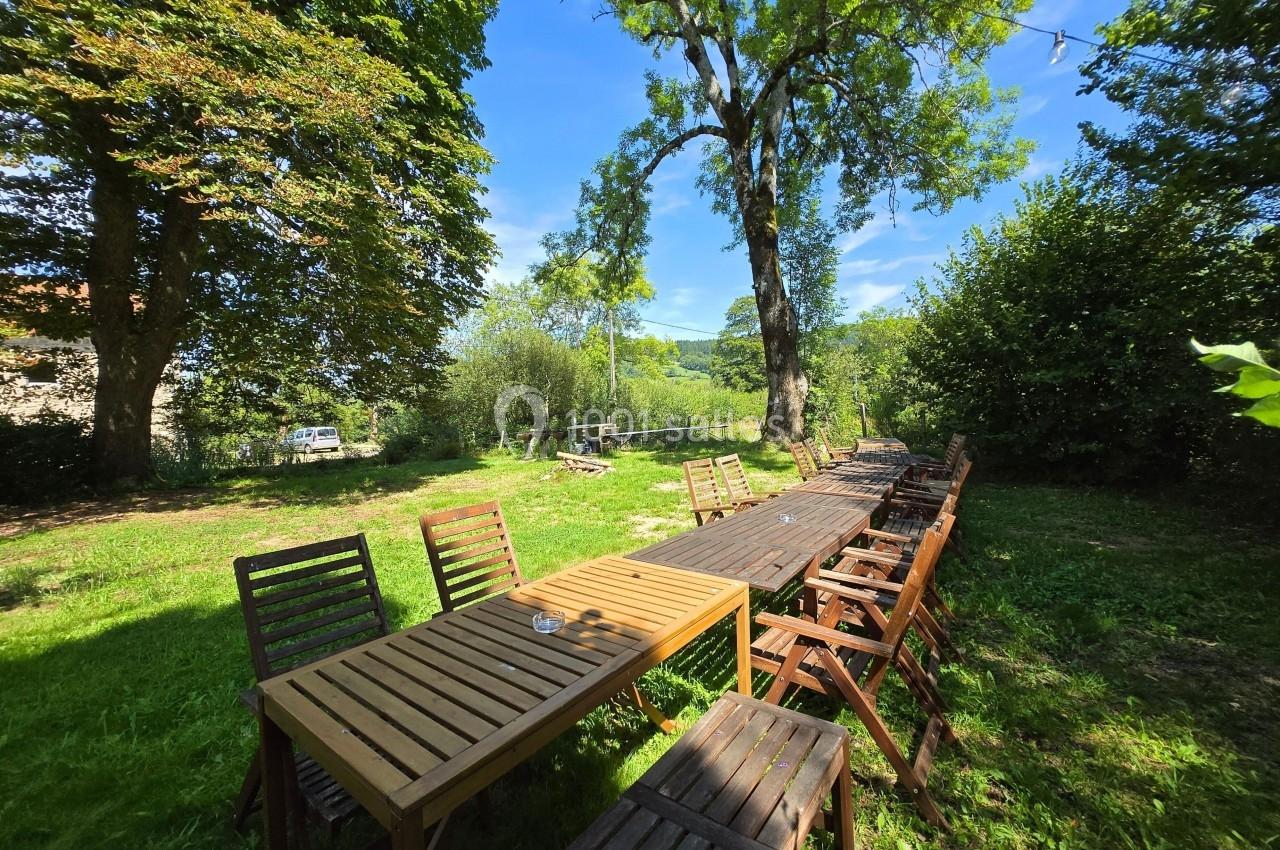 Tables et chaises en bois disposées en extérieur dans un jardin verdoyant sous un ciel bleu.