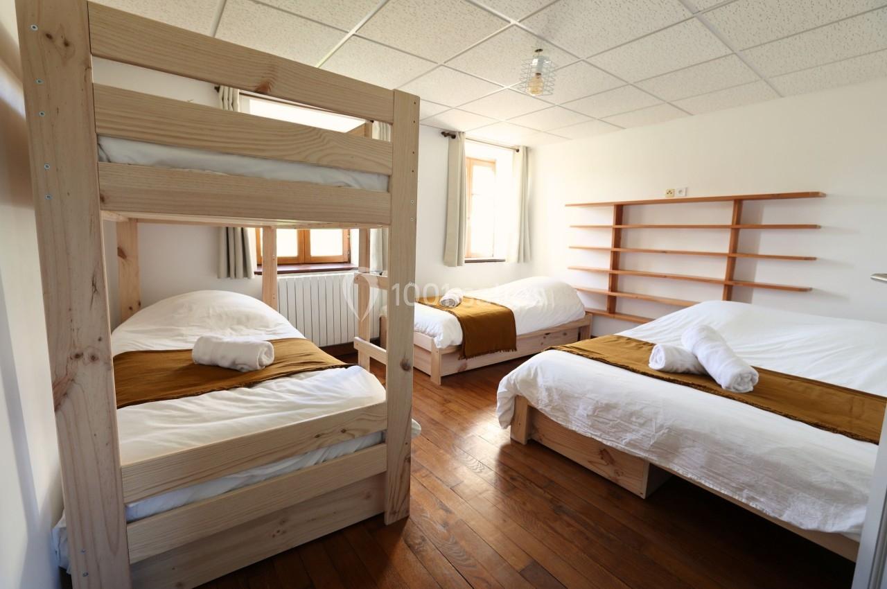 Chambre lumineuse avec trois lits simples, dont un superposé, parquet en bois et étagères murales.