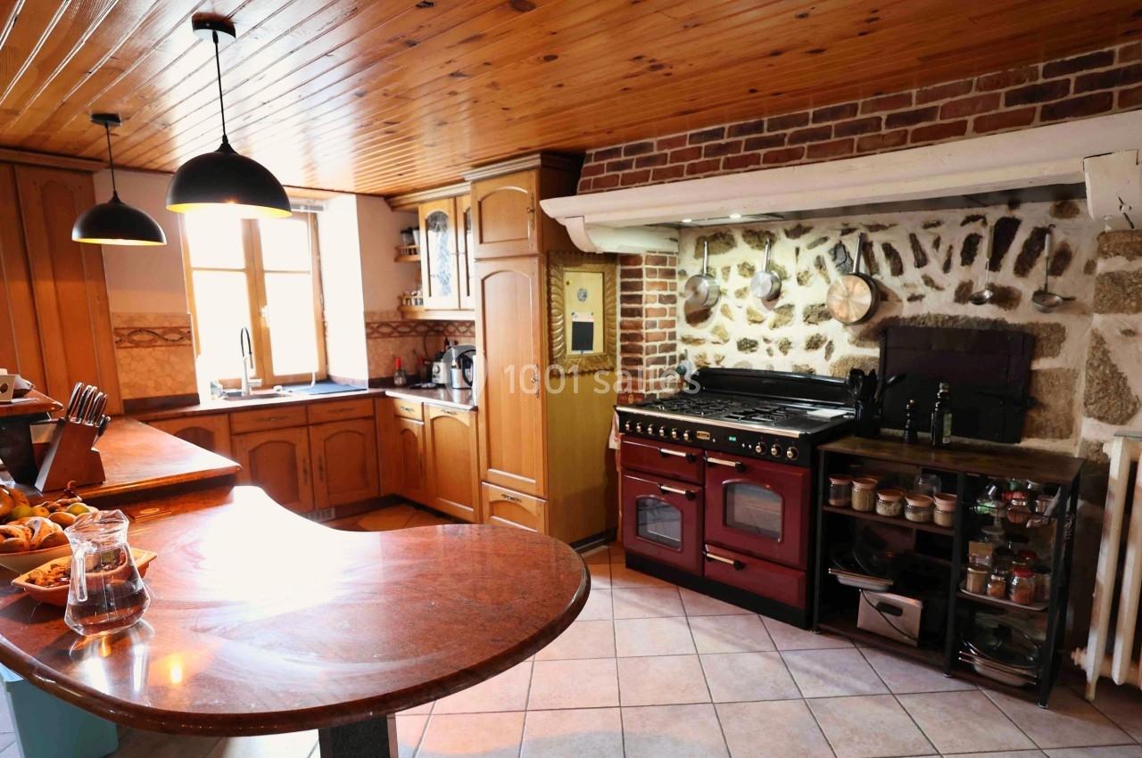 Cuisine rustique avec plafond en bois, murs en pierre et briques, grand fourneau, et plan de travail en bois.