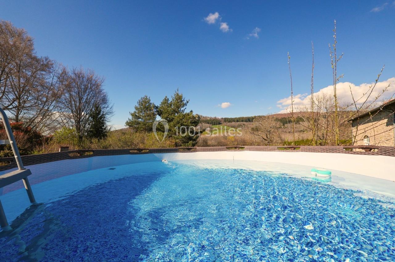 Piscine extérieure ronde avec eau bleue, entourée de végétation et d'arbres sous un ciel dégagé.