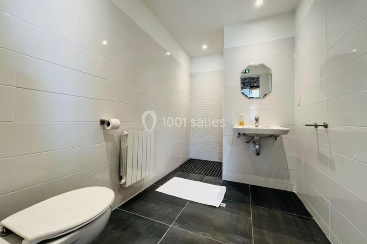 Salle de bain moderne avec toilettes, lavabo, miroir, sol sombre et murs carrelés blancs.