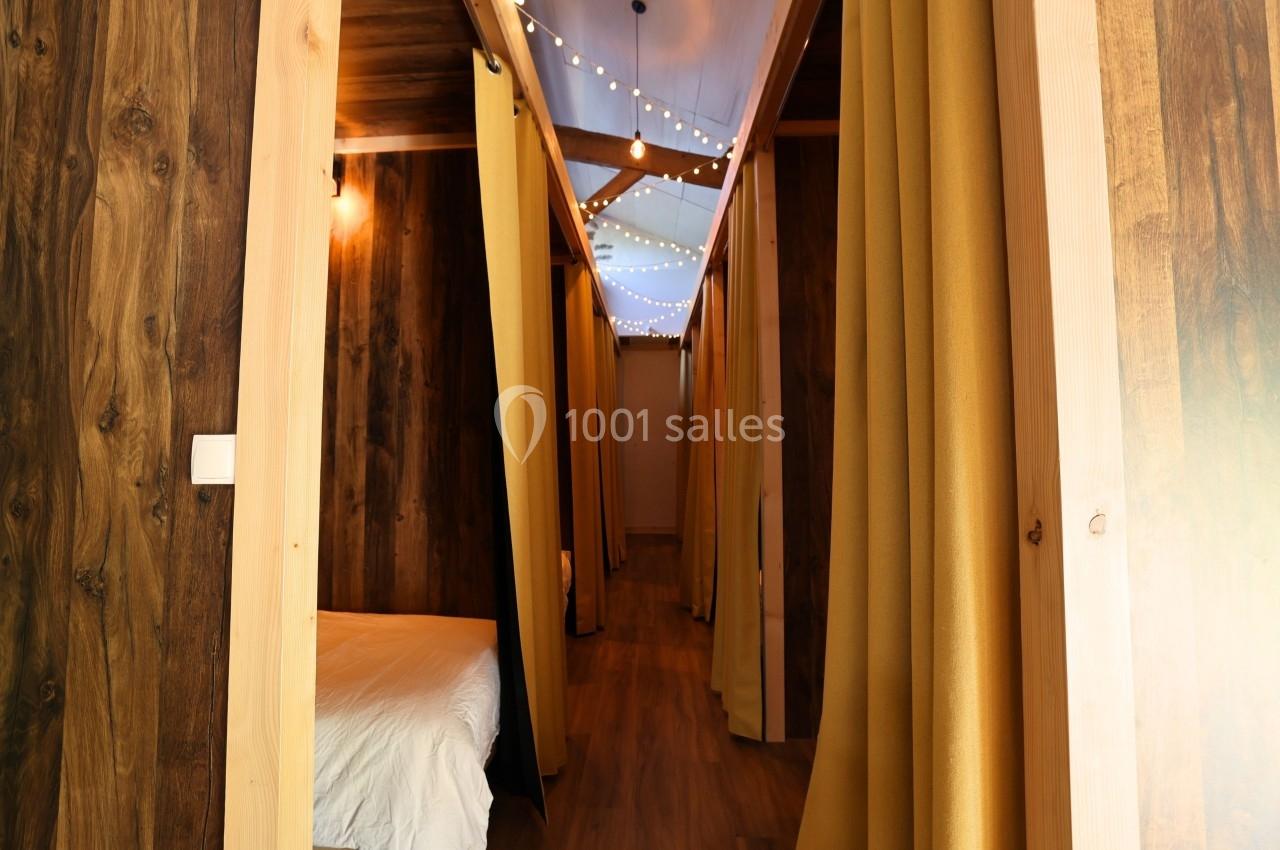 Couloir en bois avec rideaux jaunes séparant des espaces de couchage, éclairé par des guirlandes lumineuses.