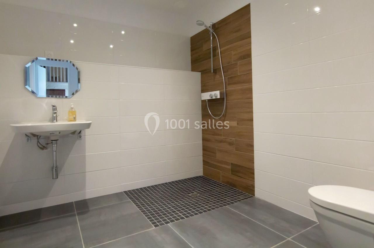 Salle de bain moderne avec douche à l'italienne, carrelage mural en bois, lavabo et miroir hexagonal.