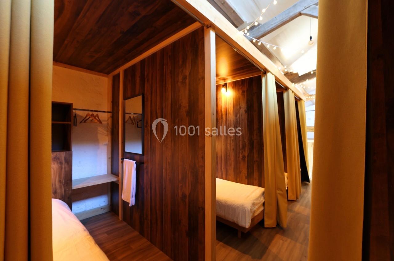 Cloisons en bois séparant des lits simples dans un dortoir avec rideaux, éclairage chaleureux et rangements intégrés.