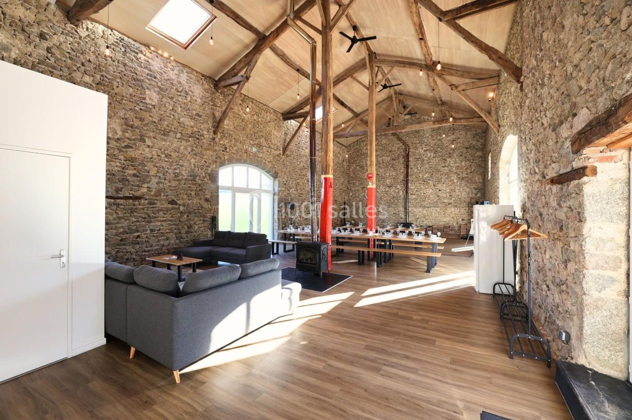 Salle lumineuse avec murs en pierre, poutres apparentes, canapés, tables dressées et parquet en bois.