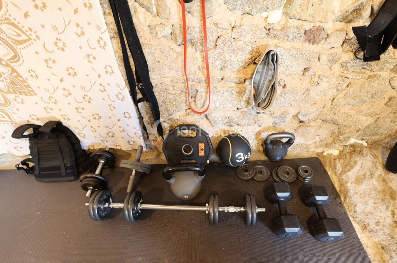 Équipement de musculation varié disposé sur un sol en mousse devant un mur en pierre.