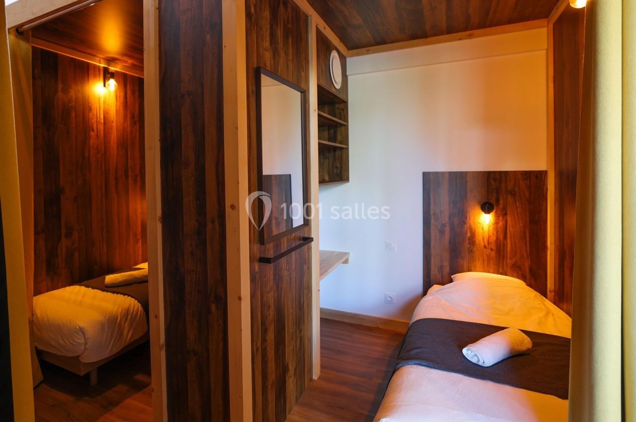 Deux lits simples dans une chambre en bois avec éclairage chaleureux et une serviette pliée sur l'un des lits.