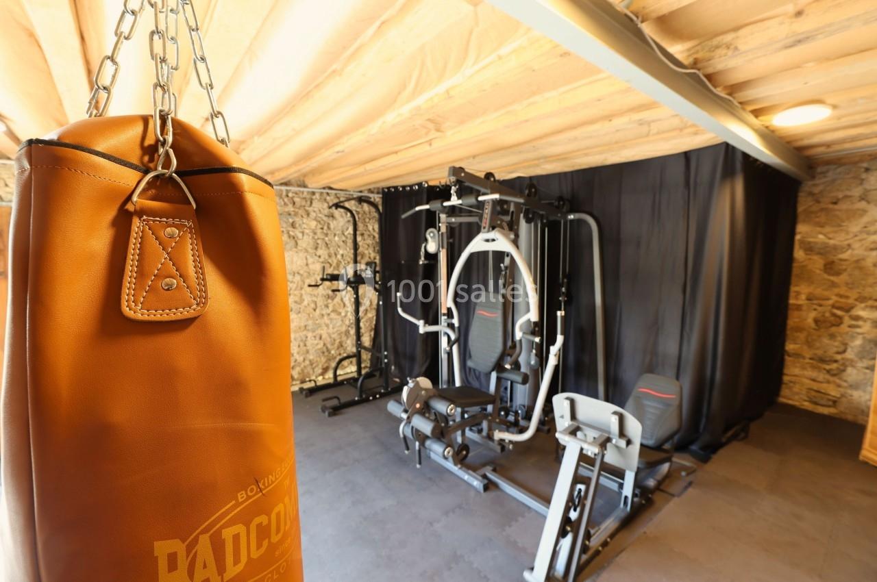 Salle de sport avec un sac de boxe en cuir au premier plan et des équipements de musculation en arrière-plan.