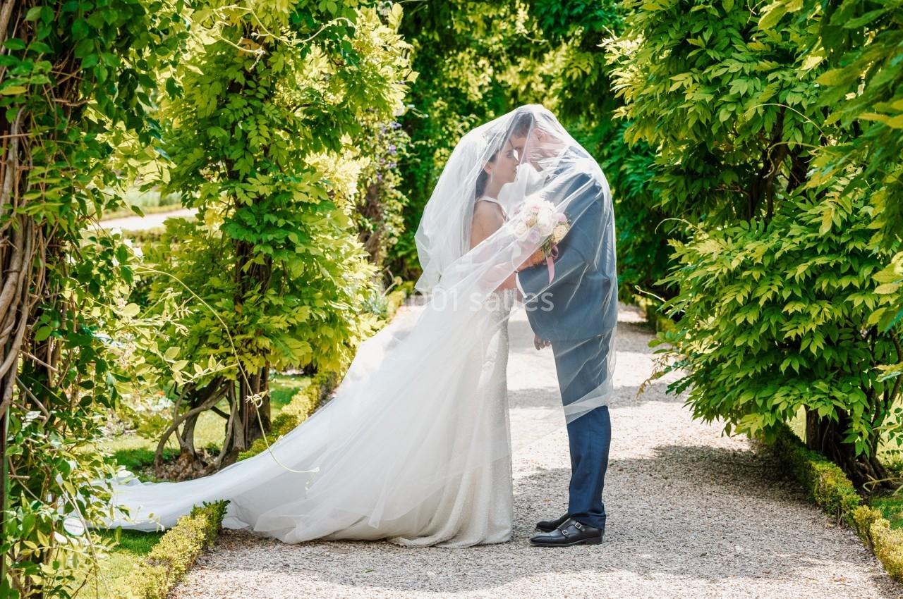 Un couple de mariés s'embrasse sous une arche végétale dans un jardin, entouré de verdure.
