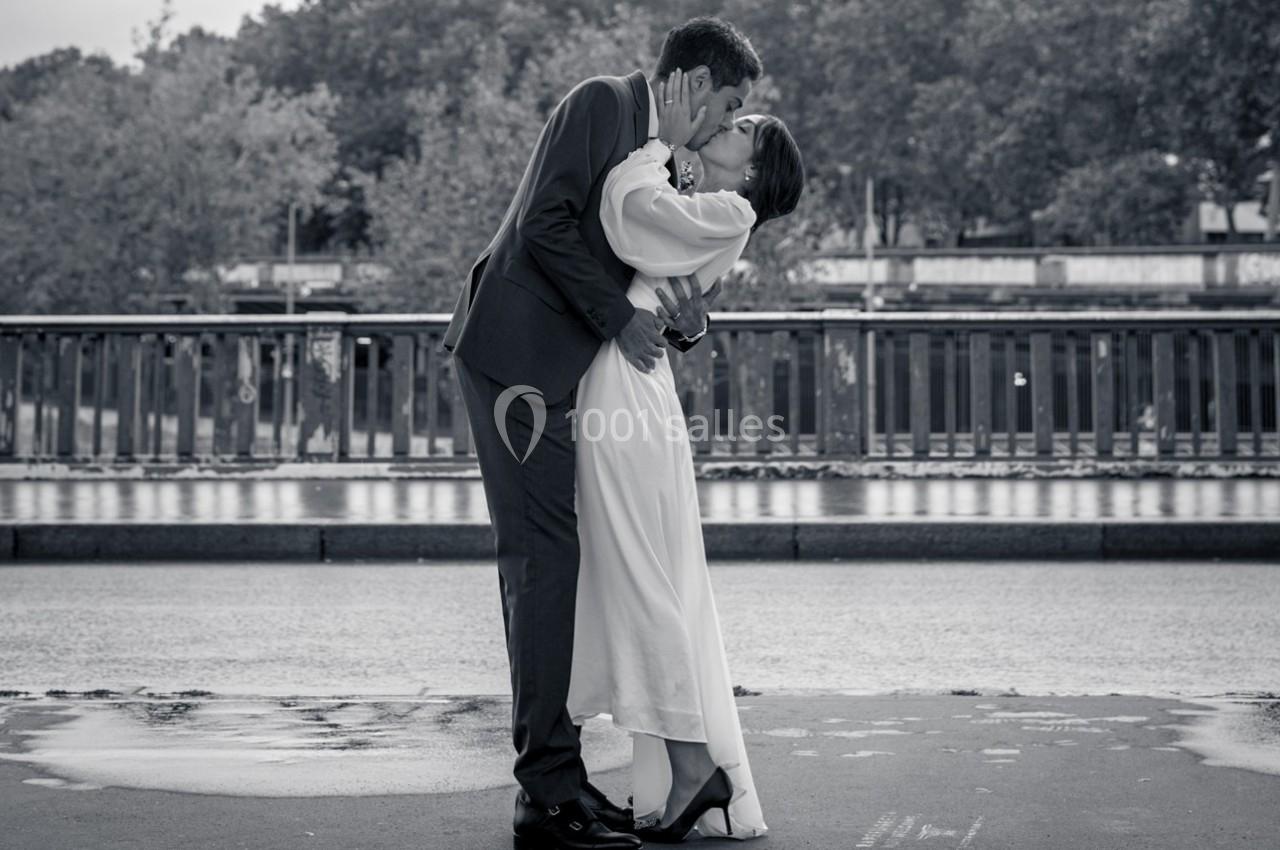 Un couple en tenue de mariage s'embrasse tendrement sur un pont, avec des arbres en arrière-plan.